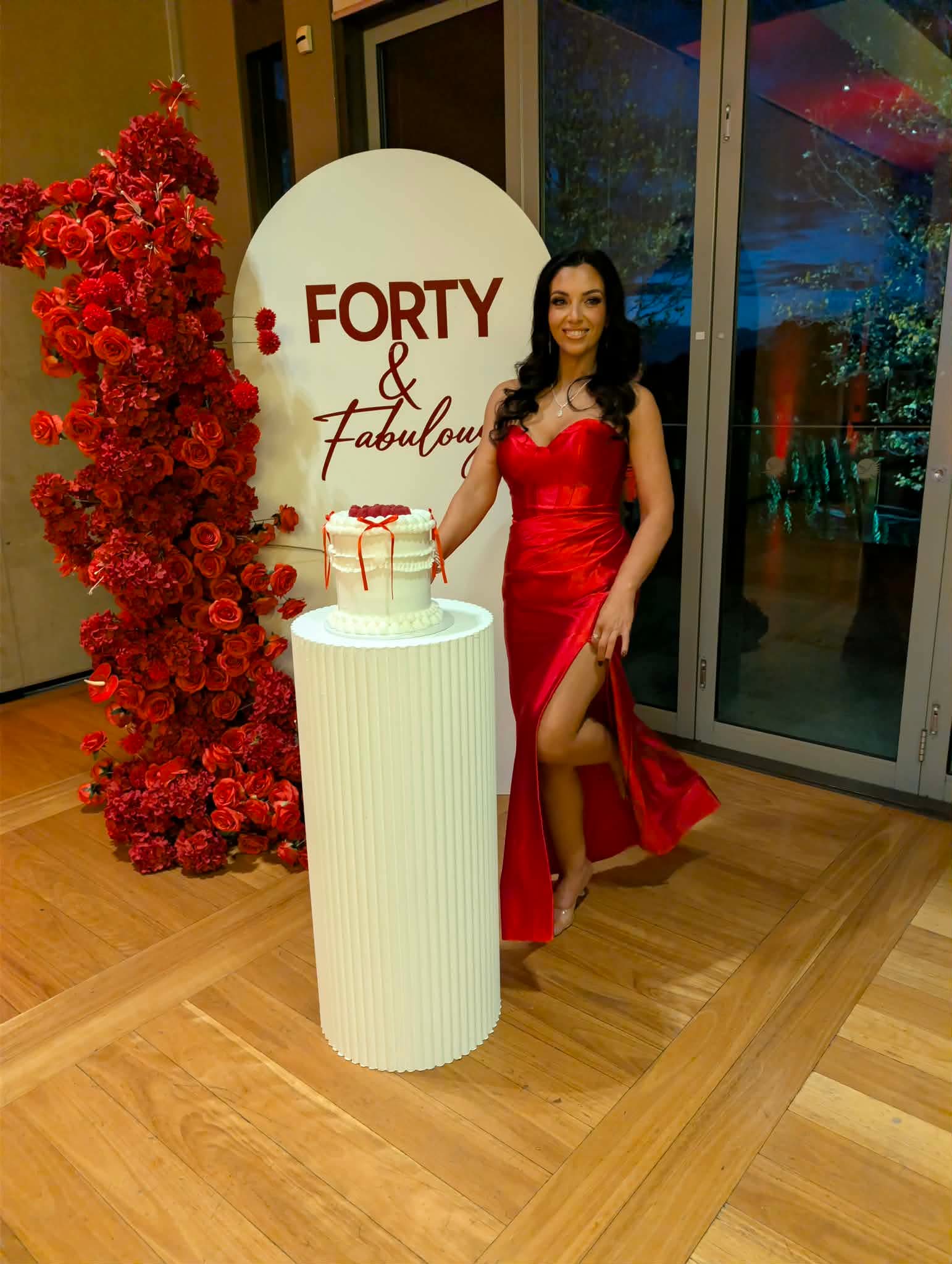 Forty and Fabulous 40th birthday setup with red floral arch, white arch backdrop and ribbed plinth