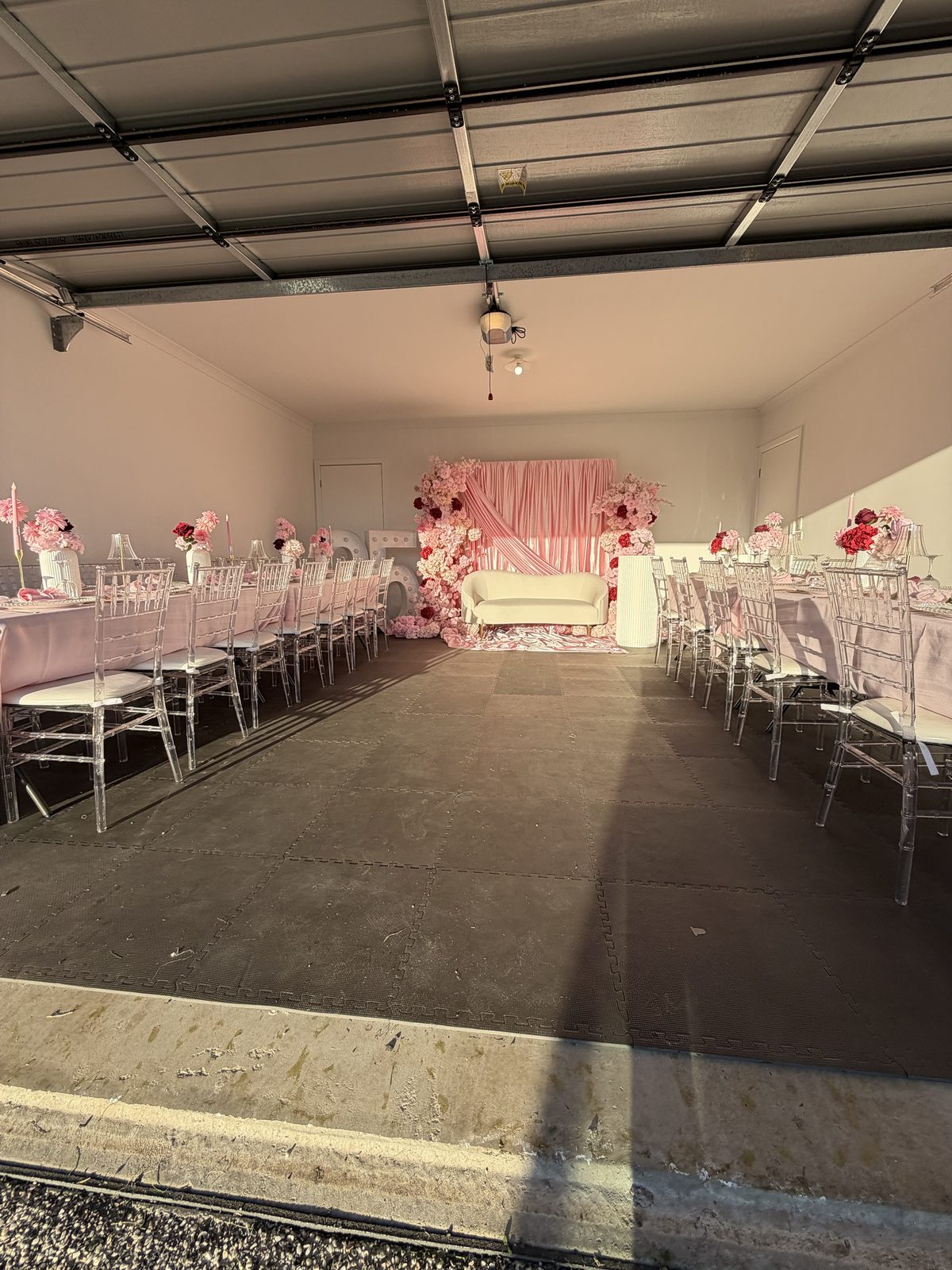 Full pink birthday setup with two long tables, clear chiavari chairs, floral columns and draped backdrop