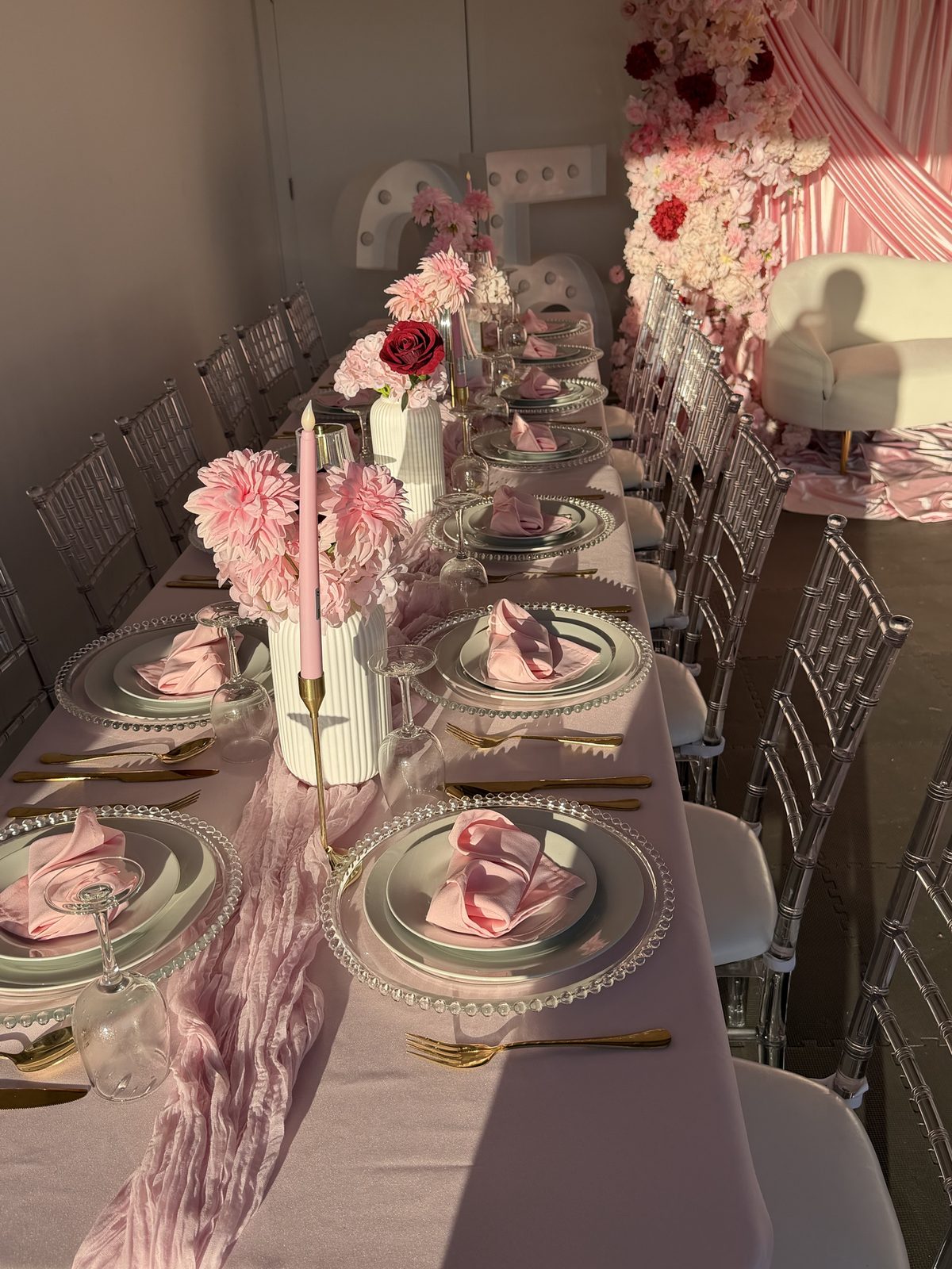 Long table styled in pink with clear chiavari chairs, beaded chargers and gold cutlery