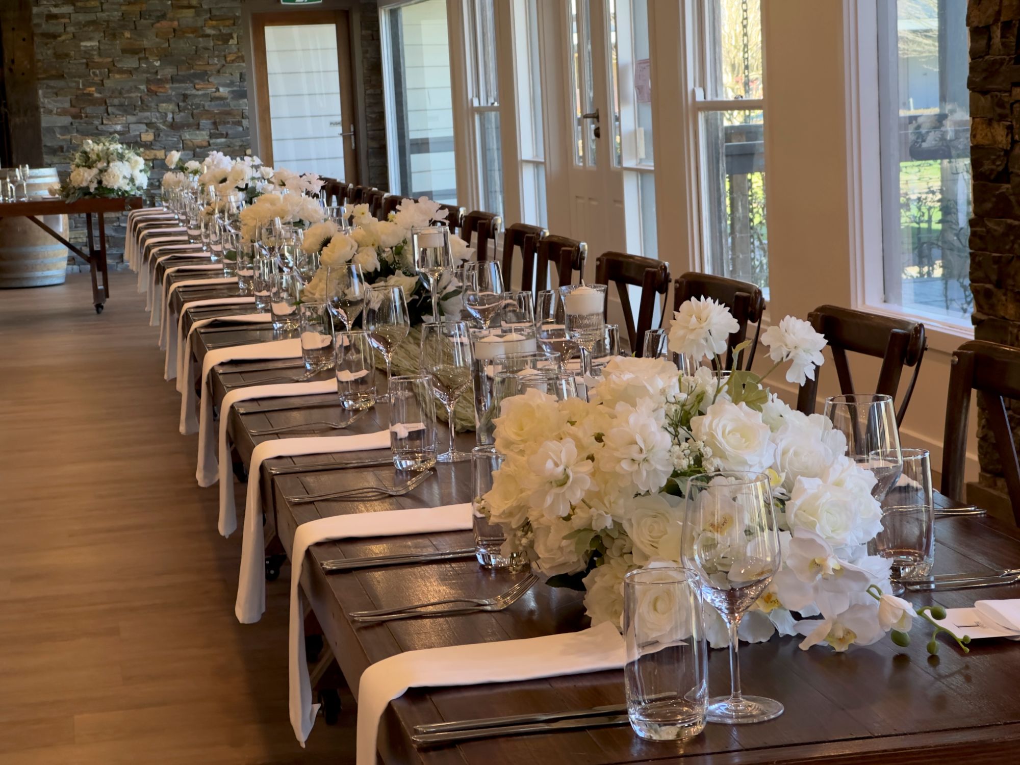 Long wedding banquet table with white floral centrepieces and timber crossback chairs