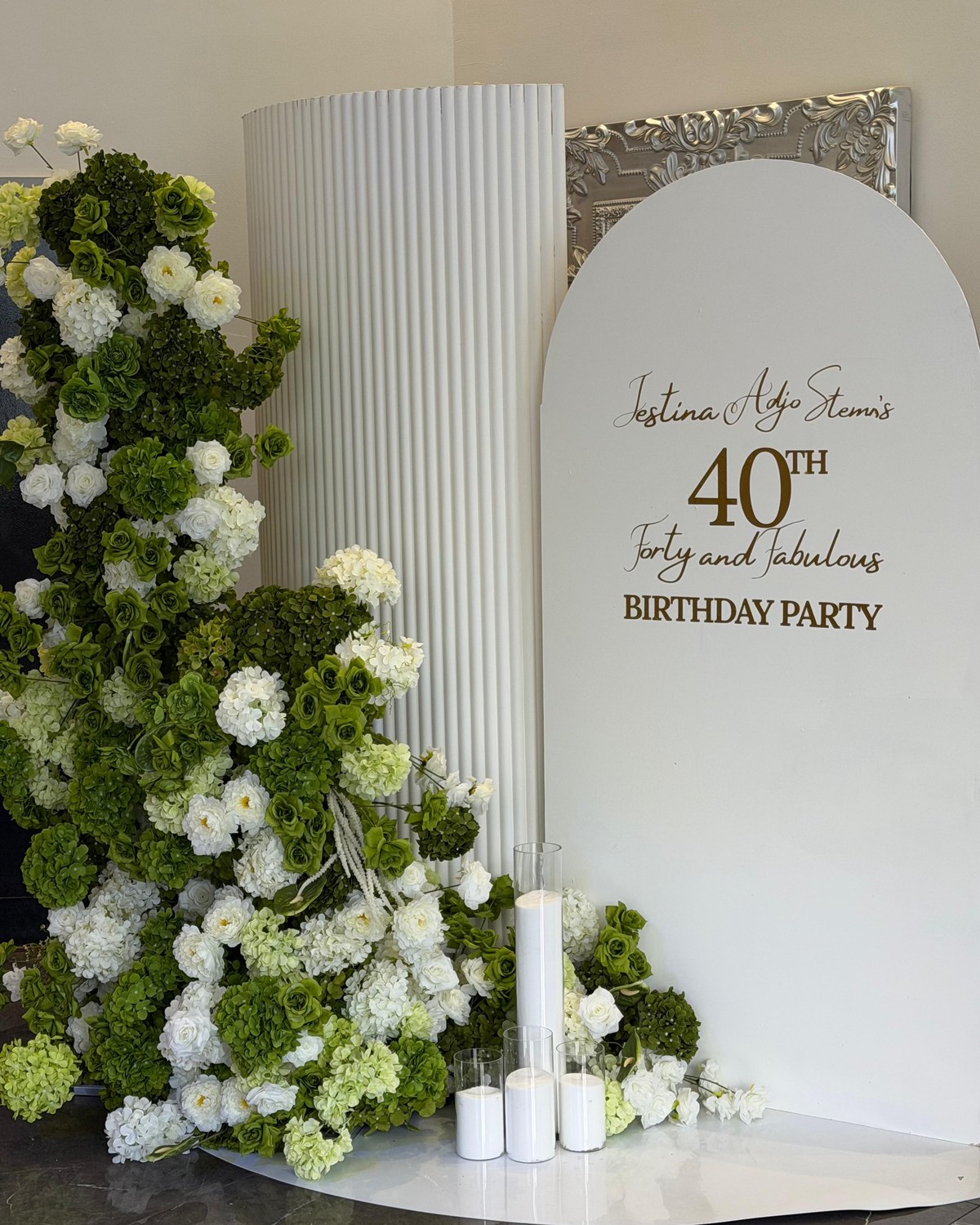Green and white 40th birthday arch backdrop with faux florals and ribbed plinth